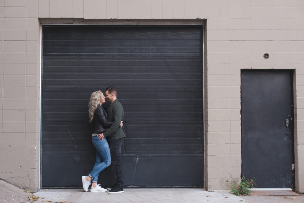 couple standing against black loading dock door kissing