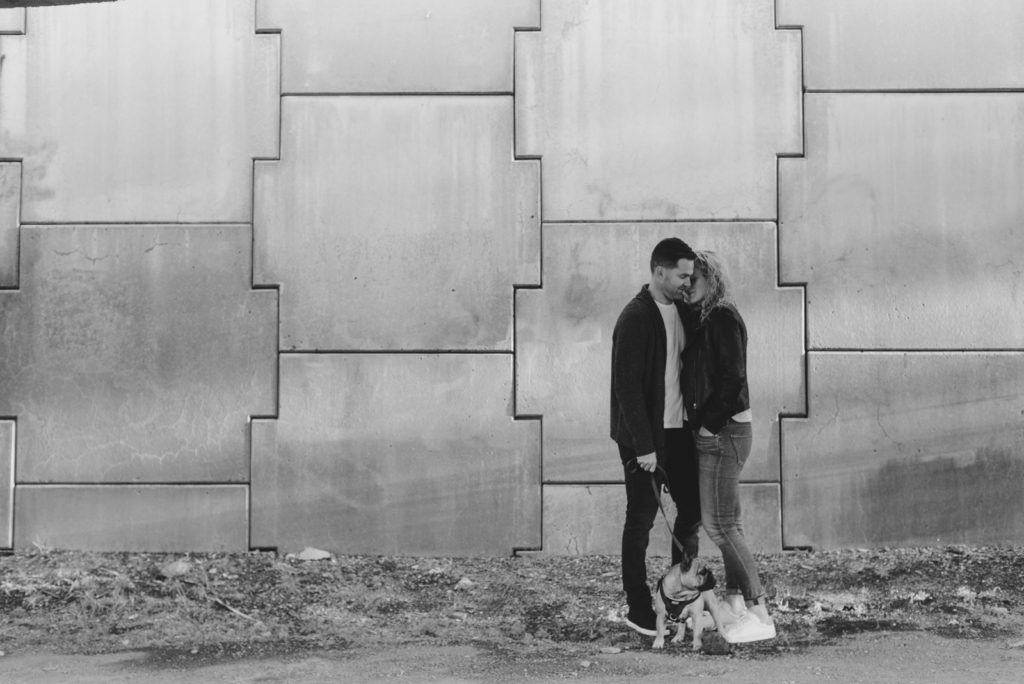 couple cuddling with their dog against geometric cement wall