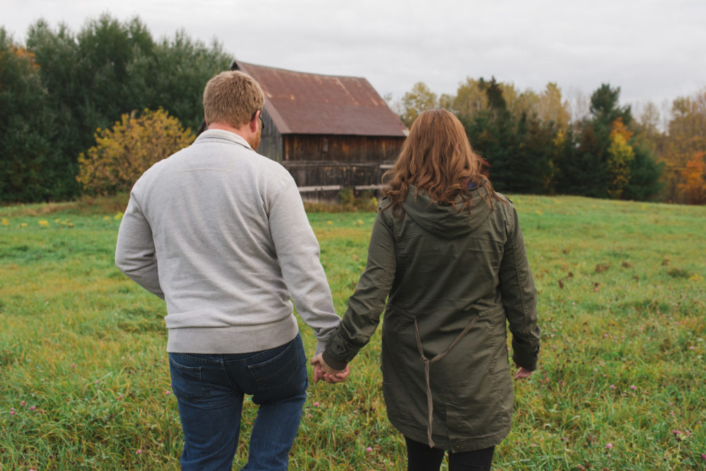 engaged couple holding hands walking towards a rustic barn