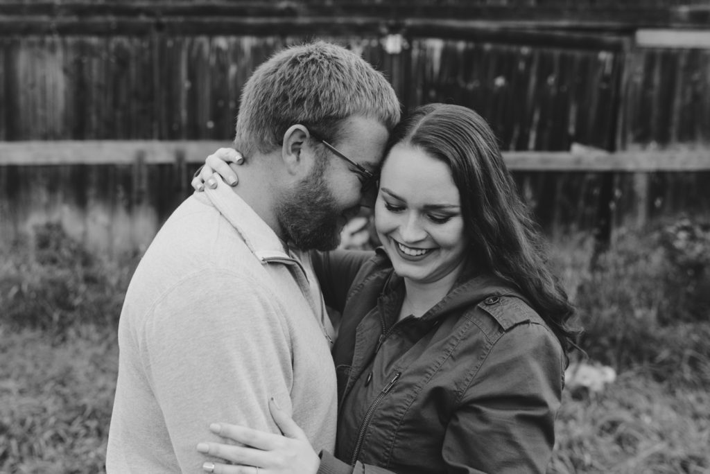 engaged couple cuddling in front of rustic barn