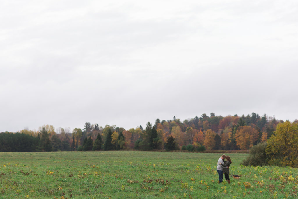 engaged couple standing in a large field with fall trees