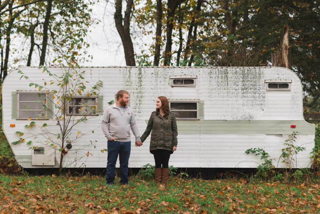 engaged couple holding hands in front of old RV trailor