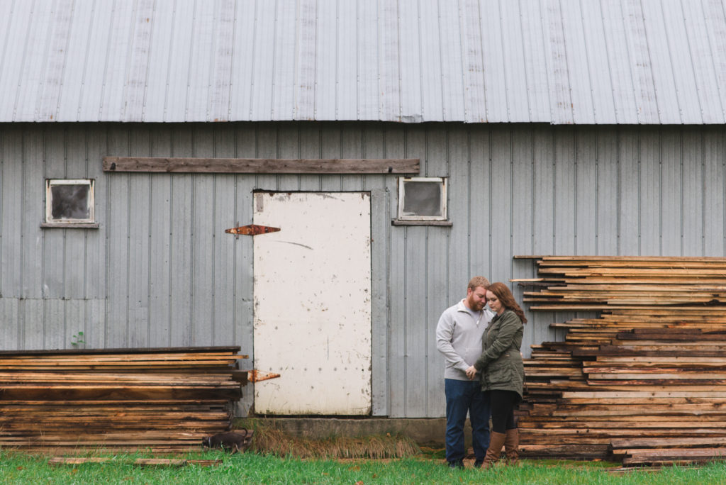 engaged couple standing in front of old barn with wooden slats
