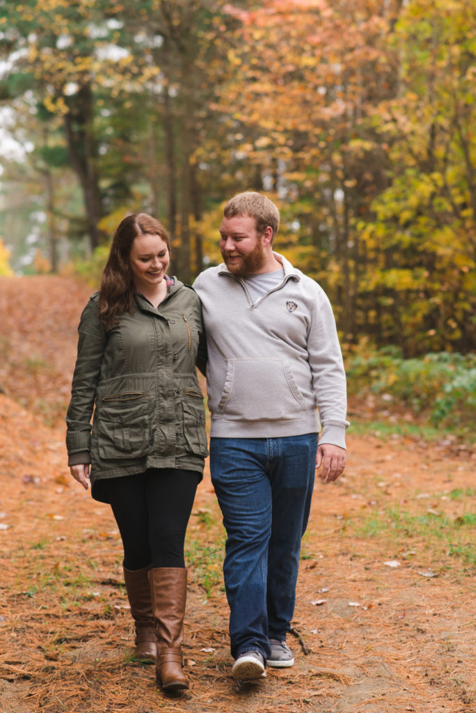 engaged couple walking together through the woods in the fall