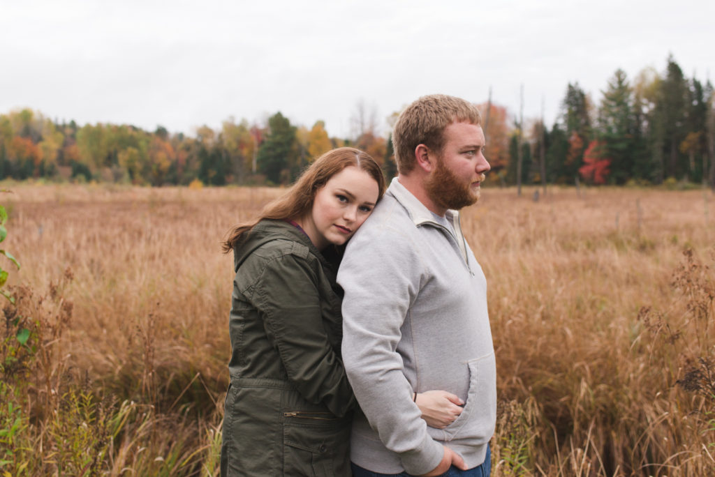 engaged couple standing in a field cuddling