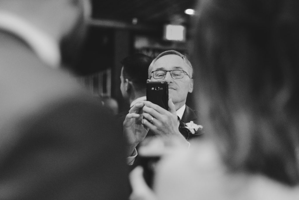 Father of the bride taking a photo of the bride and groom at the pub