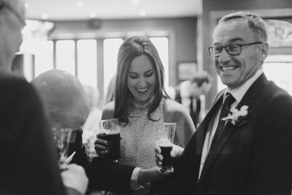 bride and her father laughing holding beers at the pub
