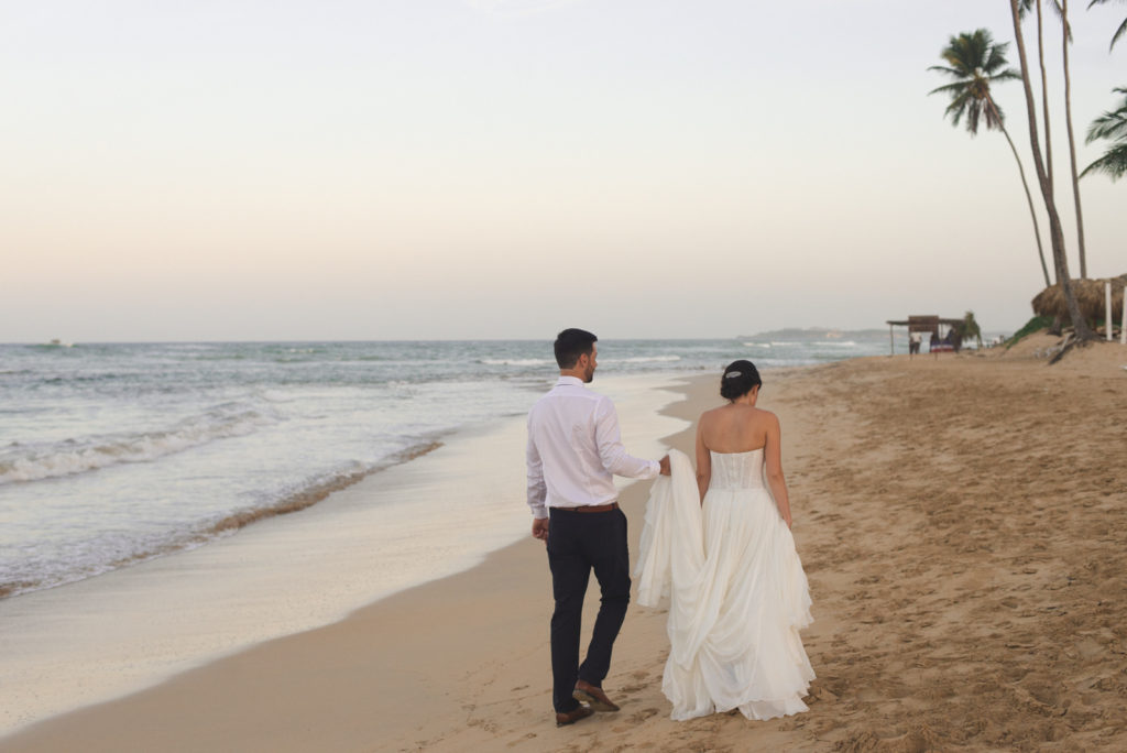 bride and groom walking down the beach together at sunset