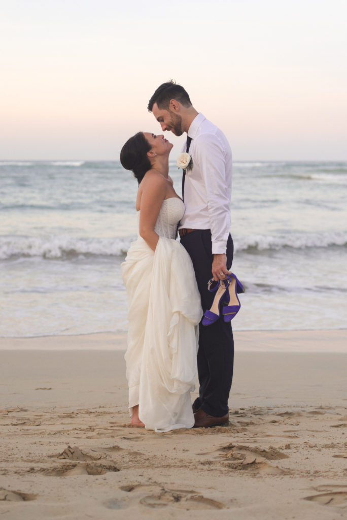 bride and groom standing on the beach at sunset