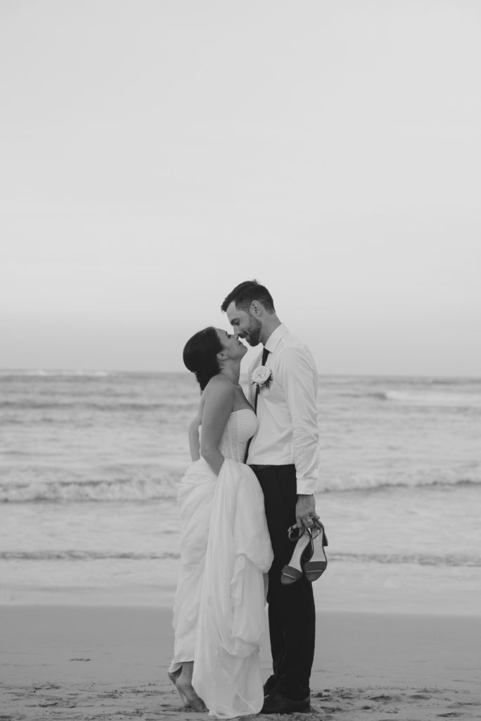 bride and groom leaning in for a kiss on the beach at sunset
