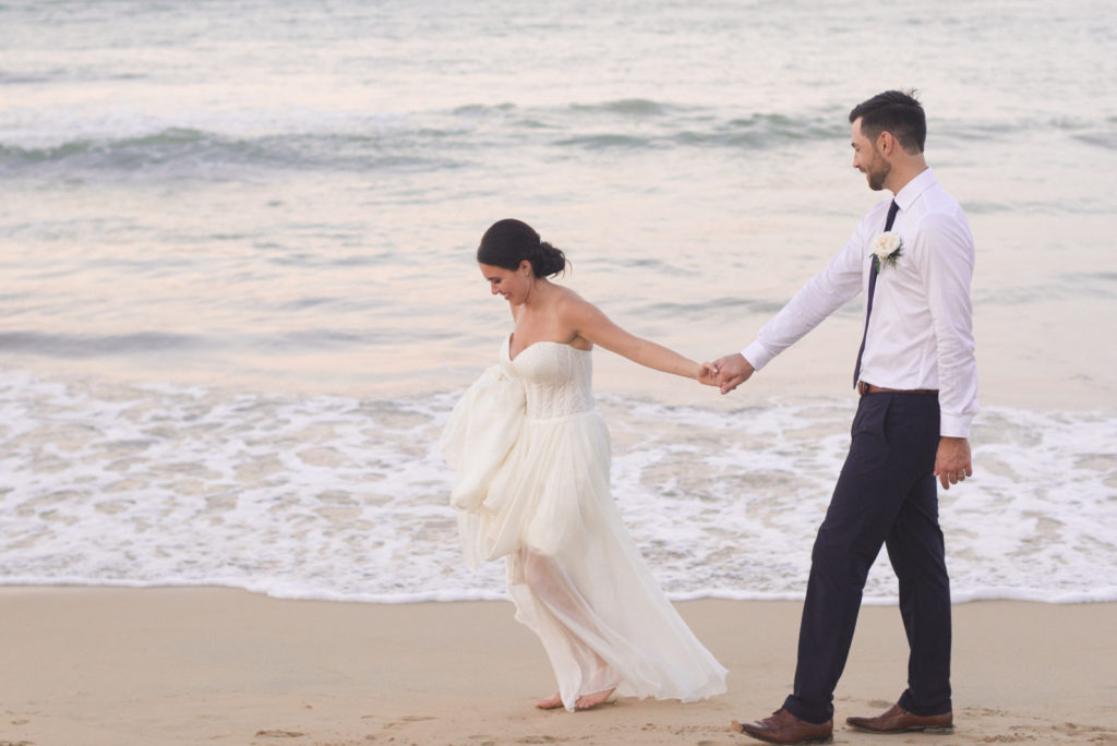 bride and groom walking along the beach together at sunset
