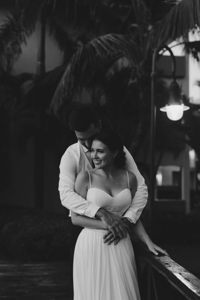 black and white photo of bride and groom standing on bridge with palm trees