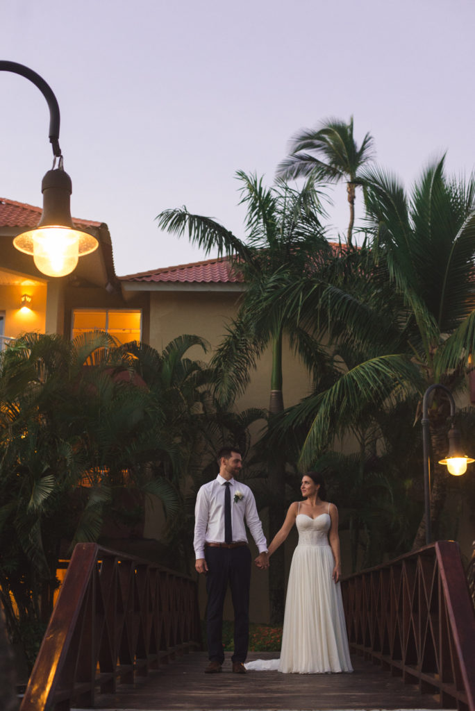 bride and groom holding hands on bridge at dusk with palm trees