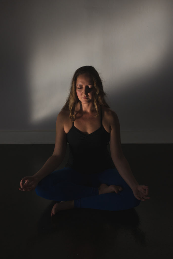 yoga teacher meditating in dark and moody window light