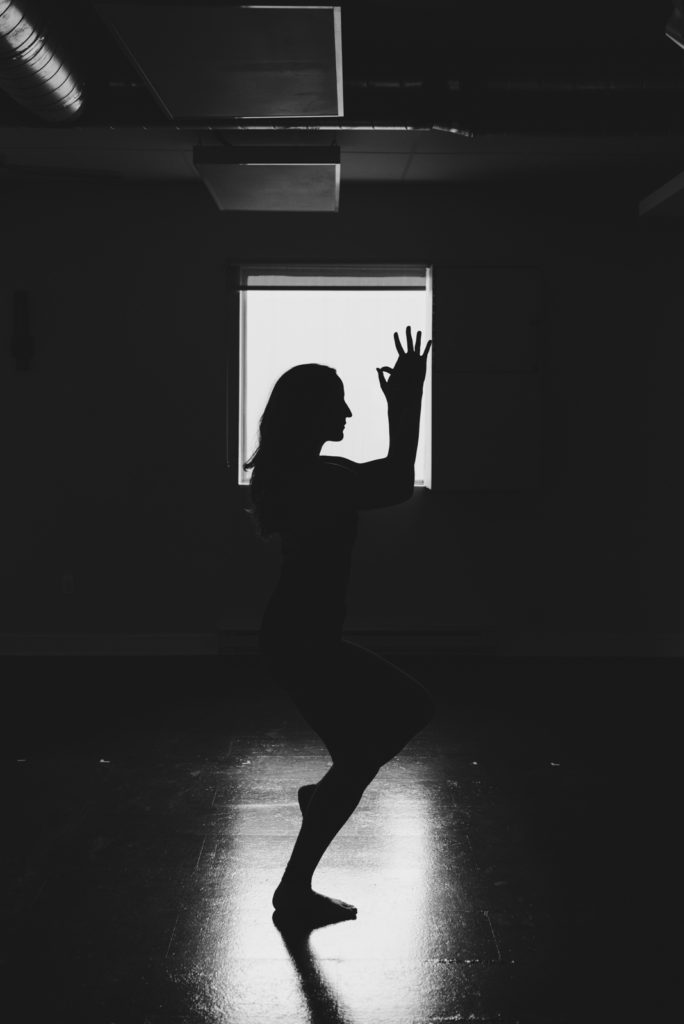 black and white silhouette of yoga teacher in eagle pose in front of window