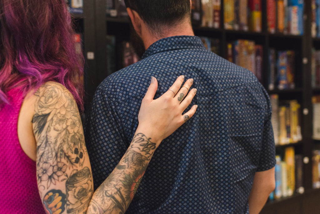 tattooed girl putting her arm around her fiancee as they look at board games