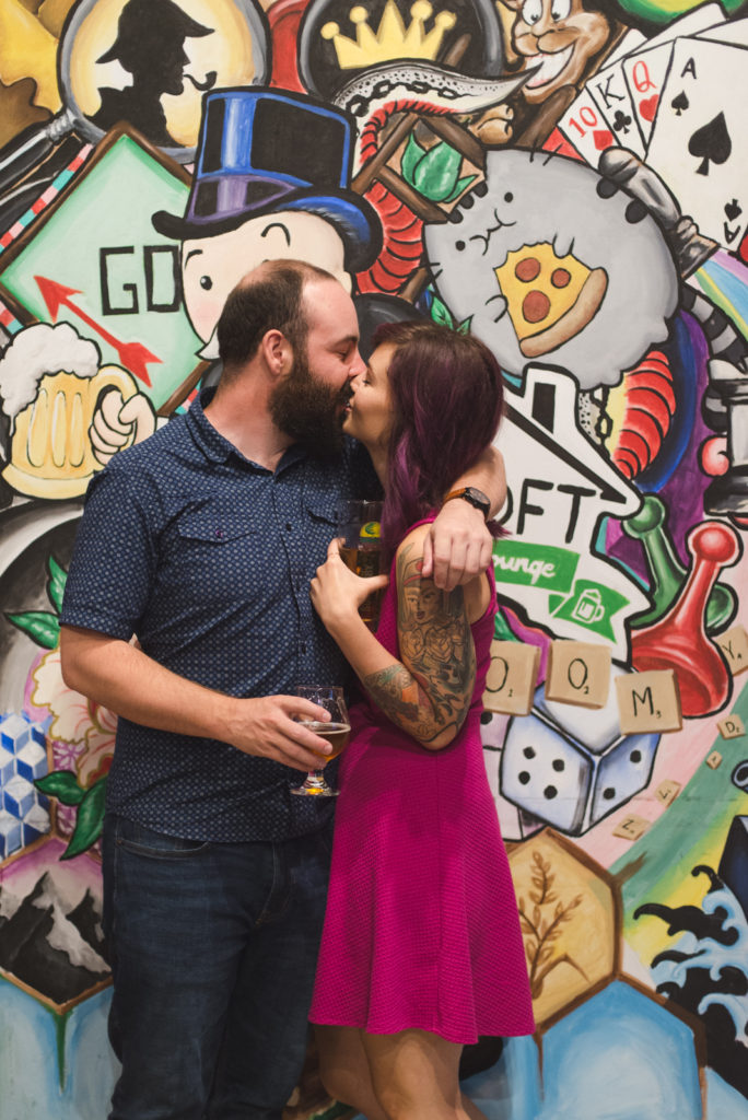 engaged couple kissing in front of mural at The Loft