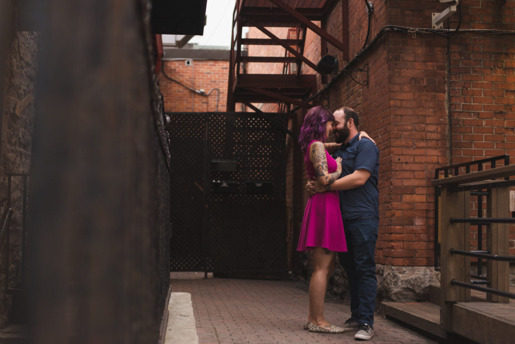 engaged couple with tattoos cuddling in alley way