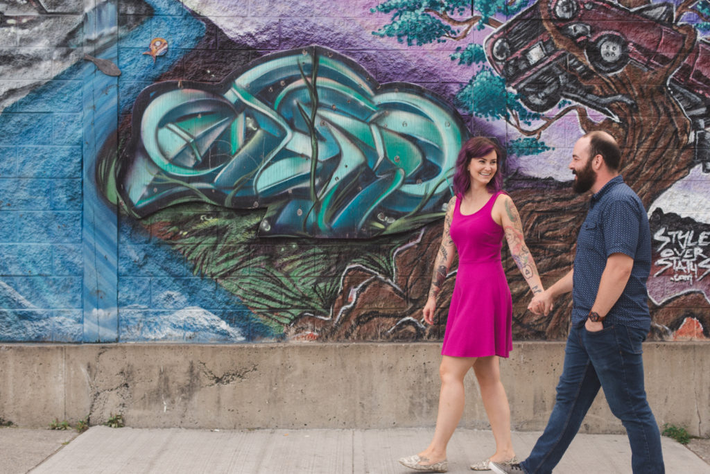 tattooed couple holding hands walking along graffiti sidewalk
