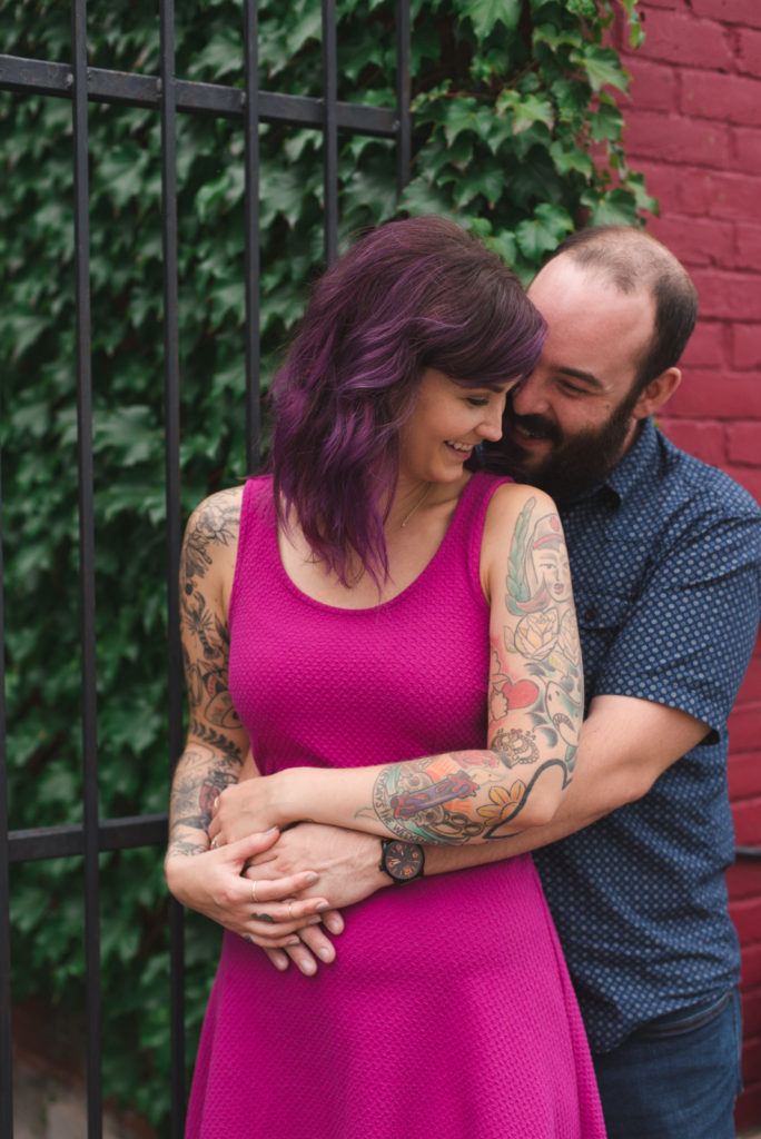 tattooed couple cuddling in front of wall with vines