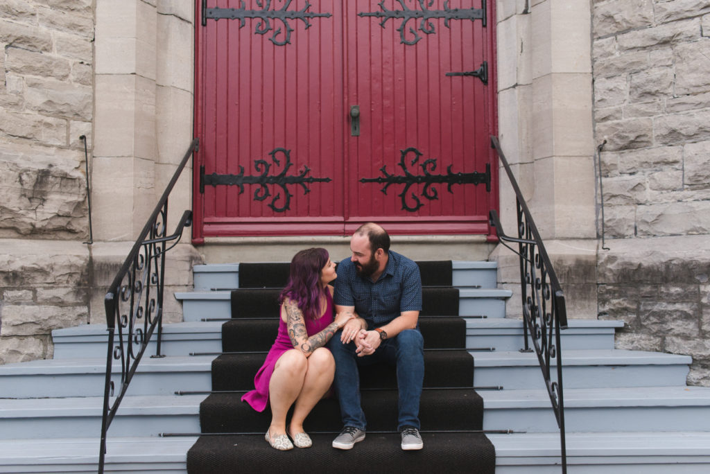 engaged couple sitting on steps of church with red door