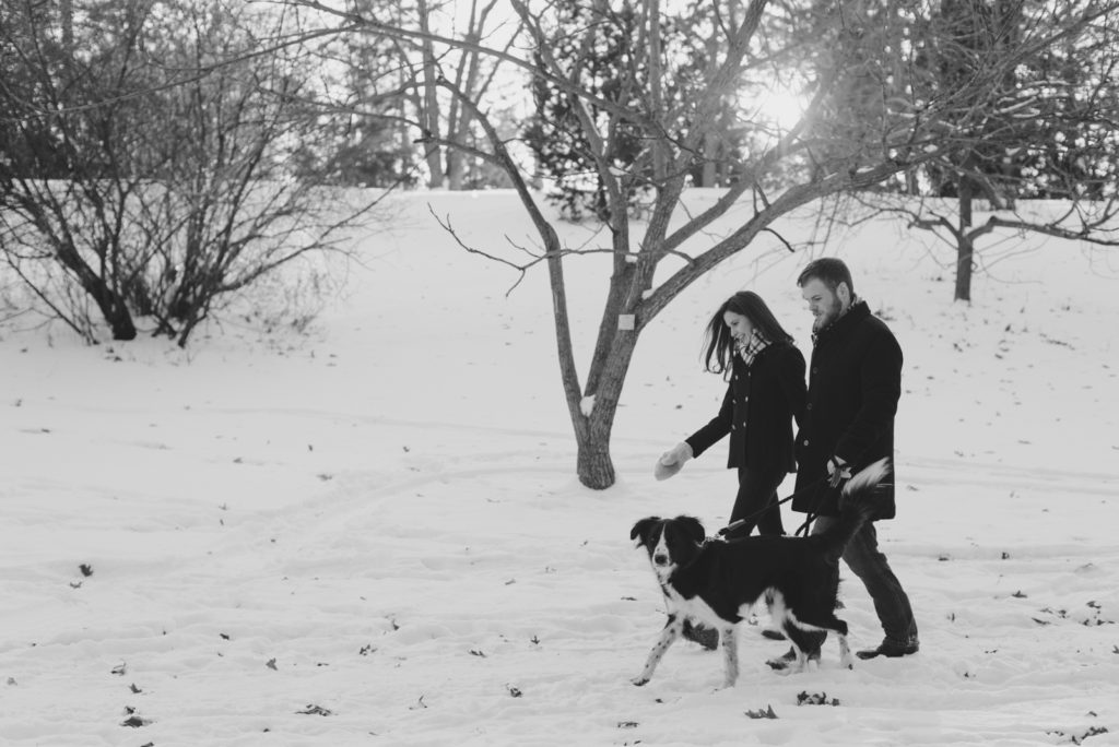 engaged couple walking in the snow with their dog