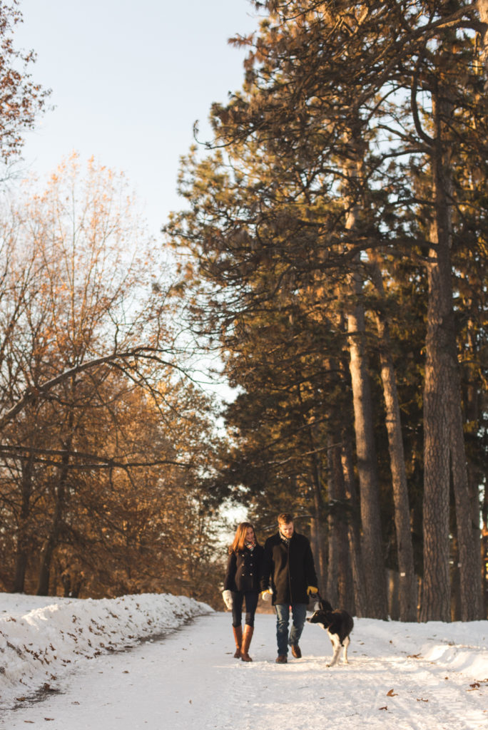 engaged couple walking down snowy path with their dog