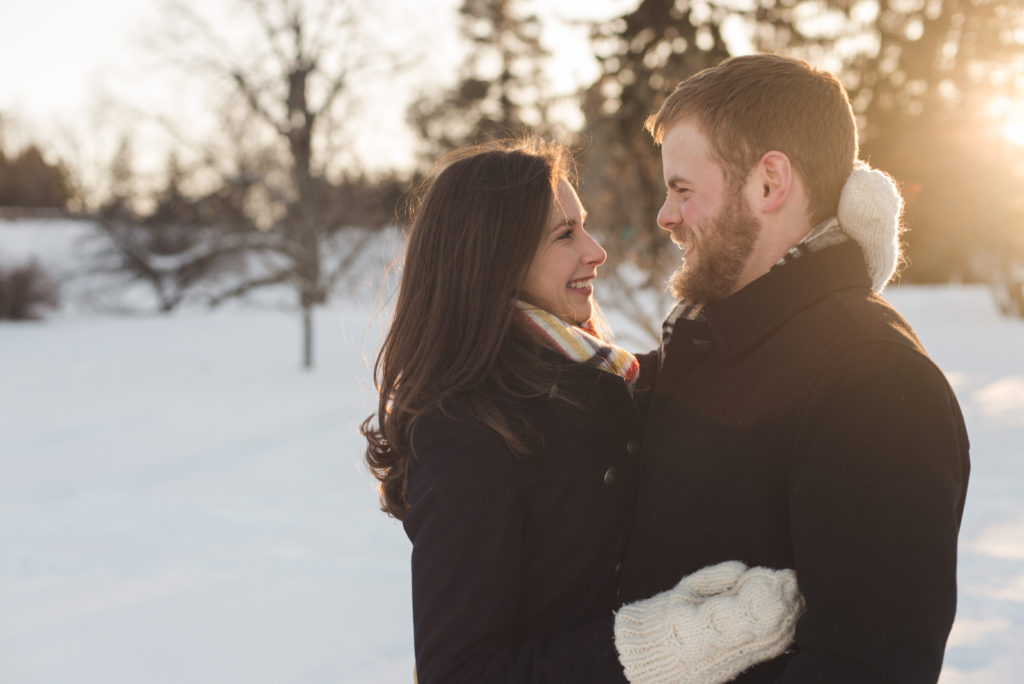 couple smiling at each other in snowy field at sunset