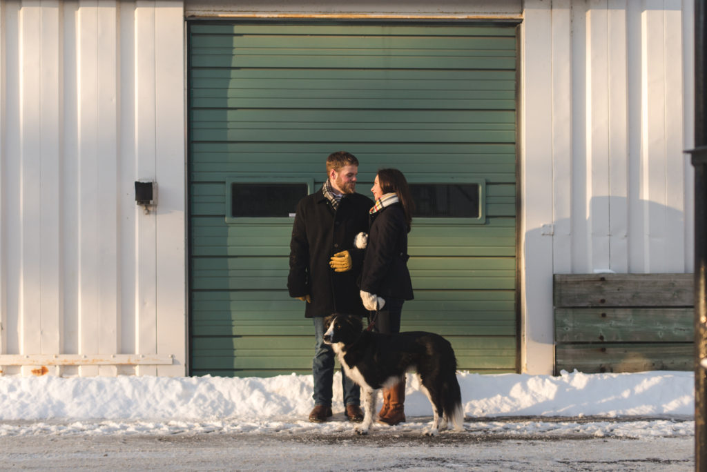 couple standing in front of green garage door with their dog at sunset