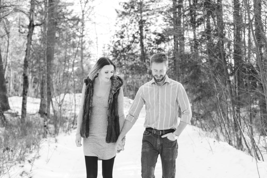 engaged couple walking along snowy wooden path