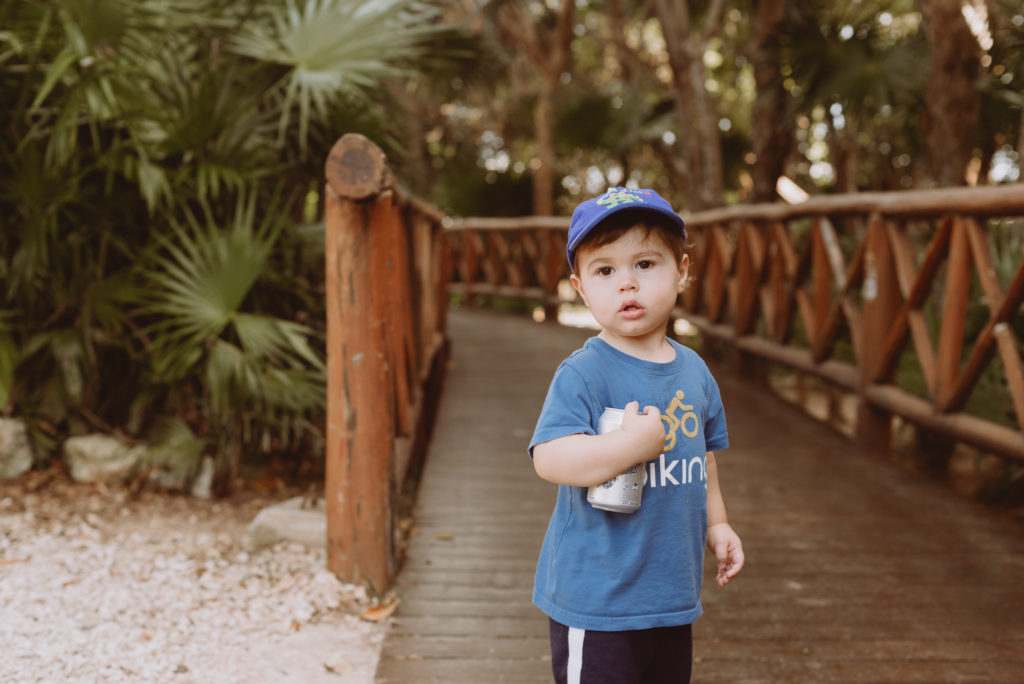 little boy standing on a wooden bridge with palm trees