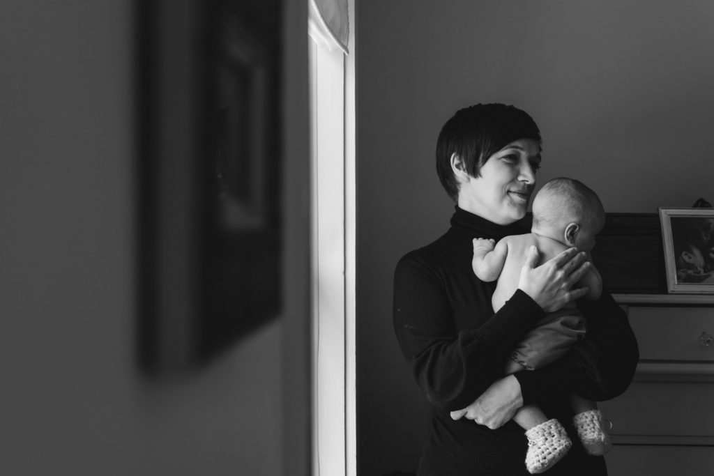 mom snuggling with baby boy in wool booties by the window in black and white