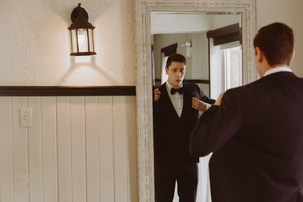groom putting on his jacket in front of the mirror
