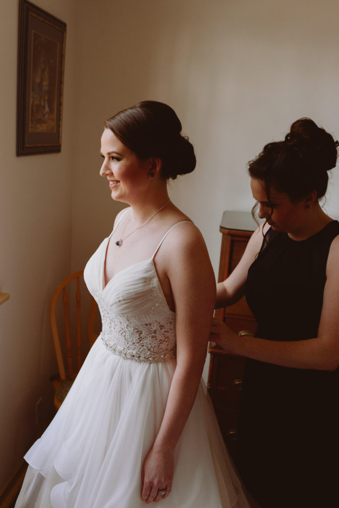 maid of honour helping bride into her wedding dress
