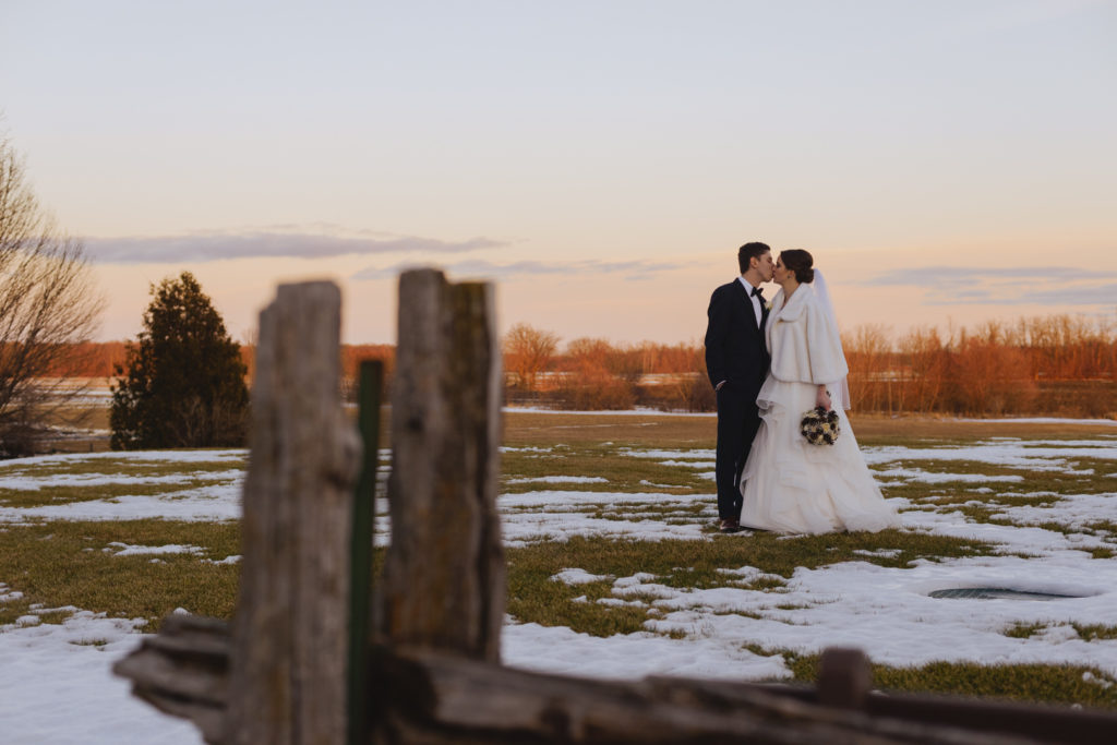 bride and groom kissing in a snowy field at sunset