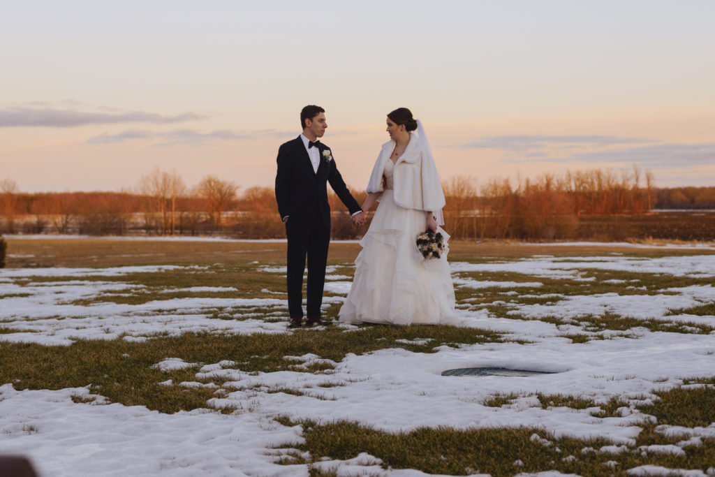 bride and groom holding hands in a snowy field at sunset