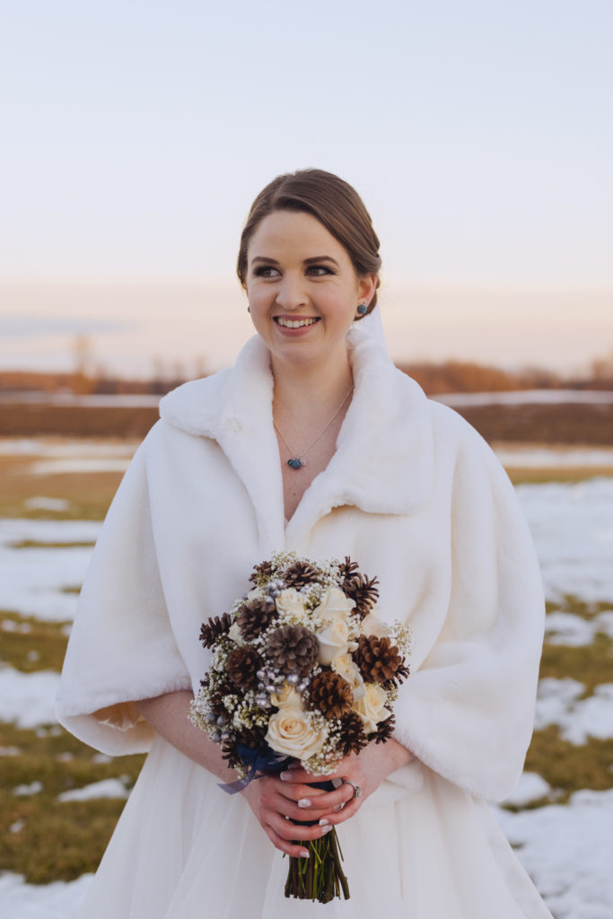 bride holding her pine cone bouquet at sunset in a snowy field