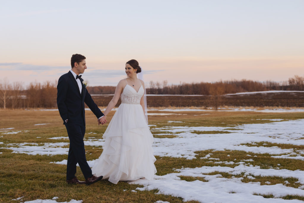 bride and groom walking in a snowy field at sunset