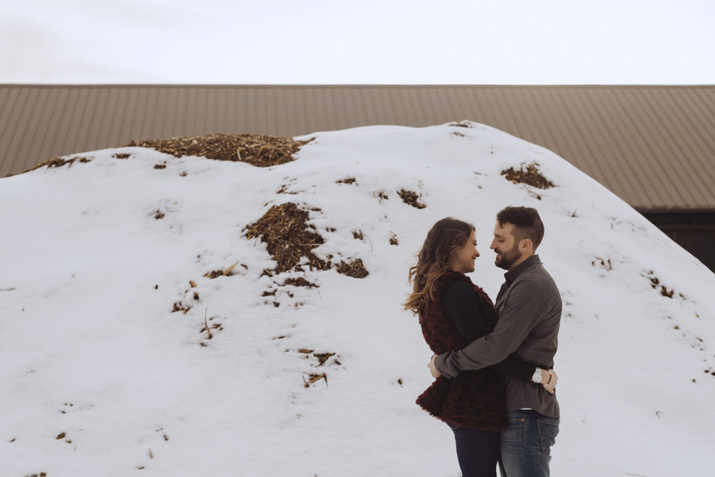 couple hugging in front of big pile of snow covered hay