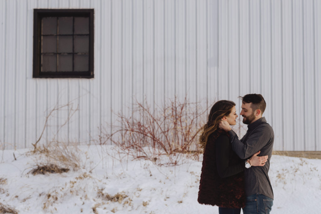couple leaning in for a kiss in front of old farm building