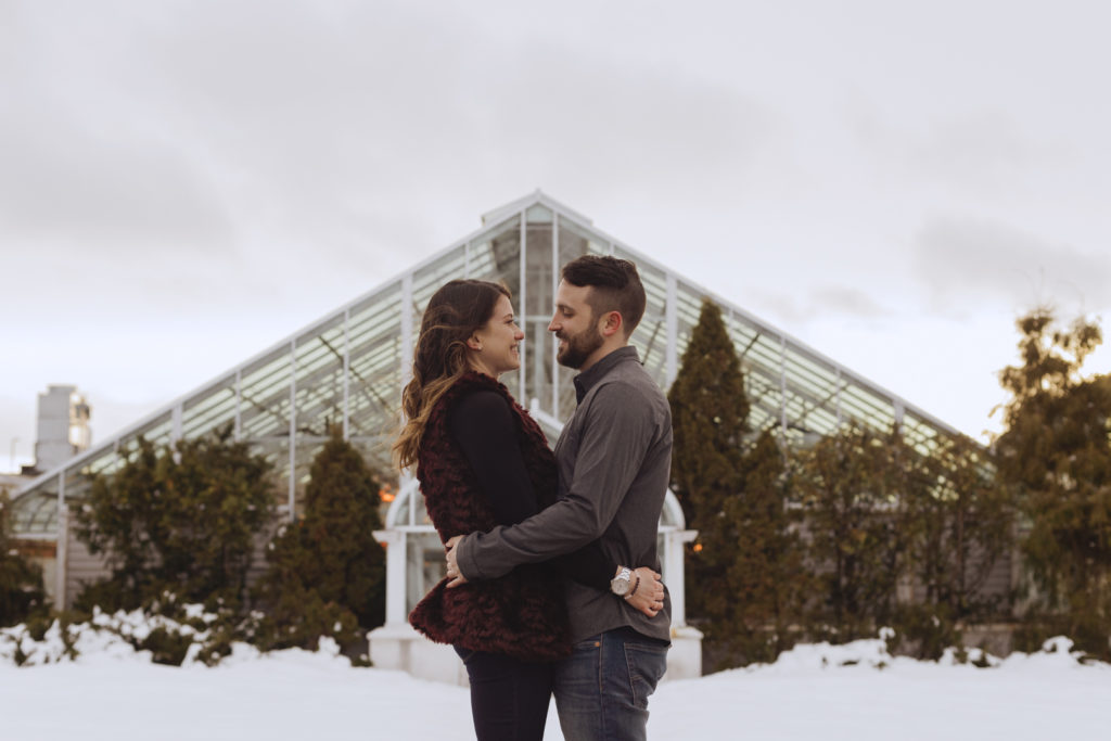 couple standing in front of greenhouse during the winter