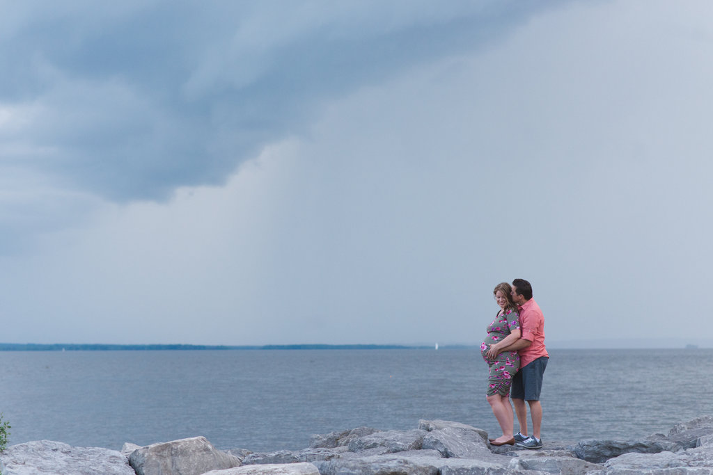 expecting parents standing by the water's edge with the rain clouds rolling in