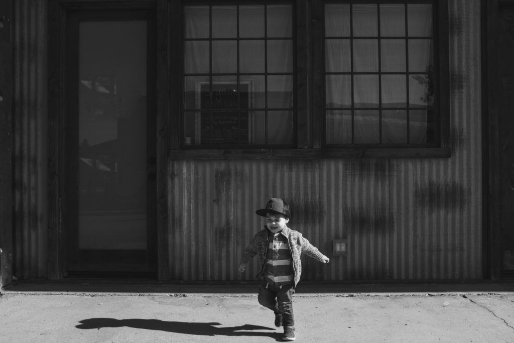 toddler running away from old metal and wood building in black and white