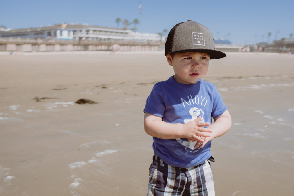 little boy wearing Billabong hat looking out into the ocean on the beach in Pismo