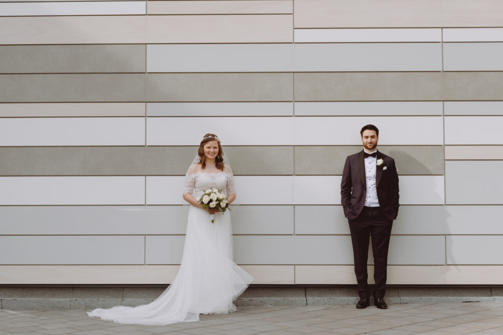 bride and groom standing against shades of grey tiled wall