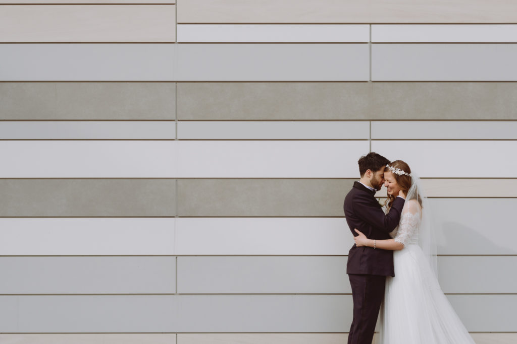 bride and groom snuggling against shades of grey tiled wall