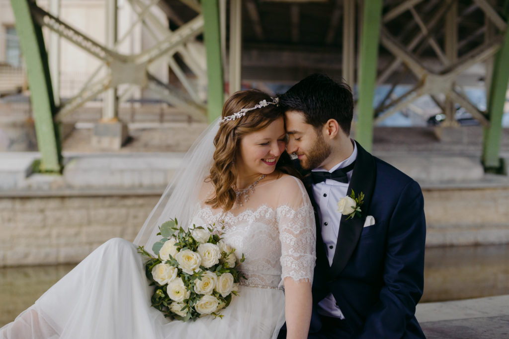 bride and groom sitting together by the canal under the laurier bridge