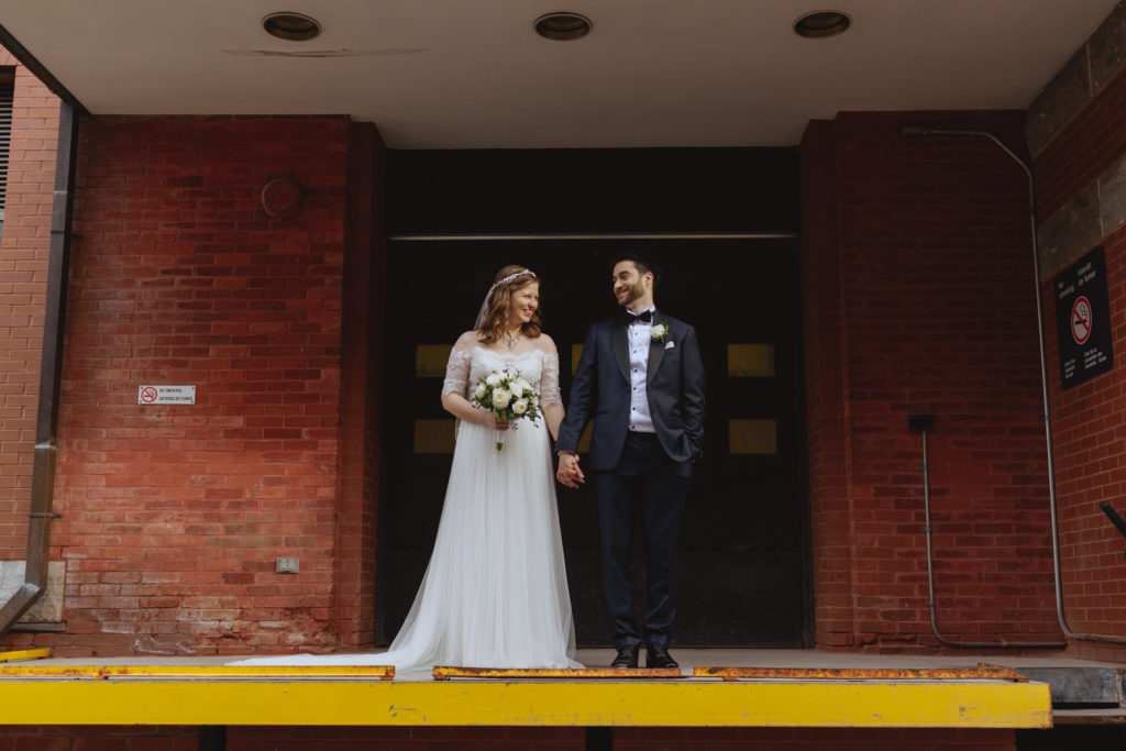 bride and groom holding hands in front of old loading dock