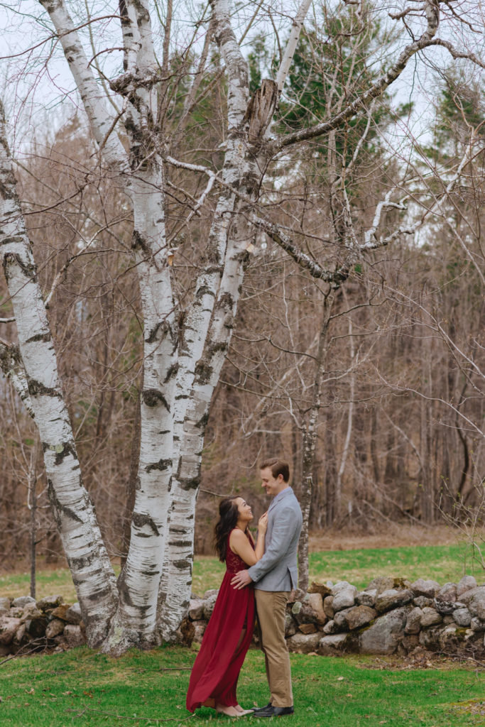 girl in a red dress cuddling her fiancee next to birch trees