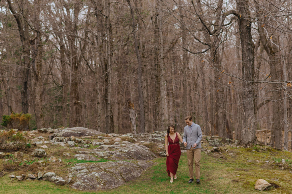 engaged couple walking together through forested path